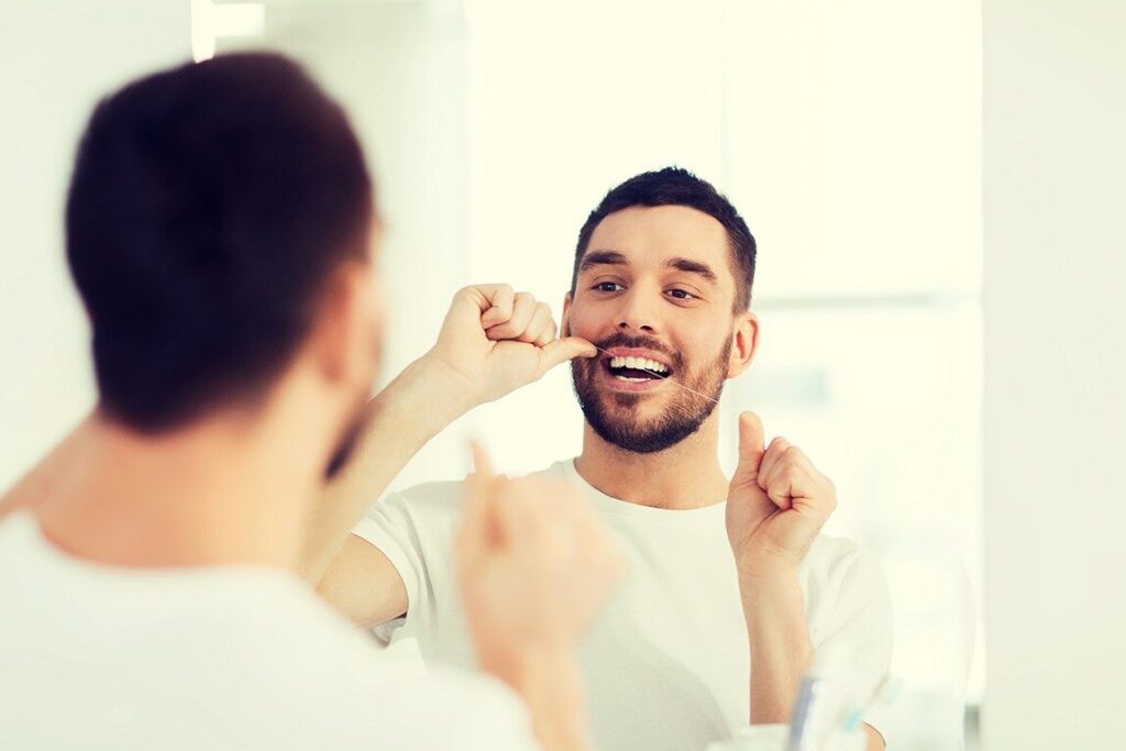 Dental Care Mistakes You Didn’t Know You Were Making 3 A person demonstrating proper flossing technique to clean the spaces between teeth