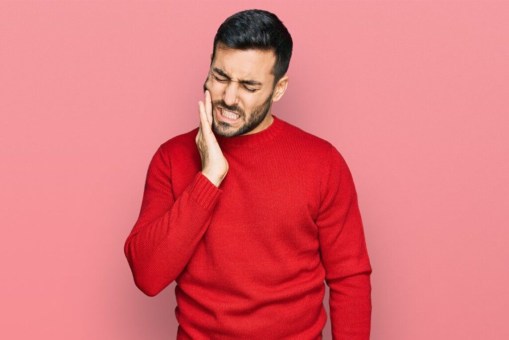 Dental Care Mistakes You Didn’t Know You Were Making 5 A person looking concerned while touching their cheek experiencing tooth sensitivity with visual indicators showing the warning signs mentioned burning sensation gum recession sensitivity