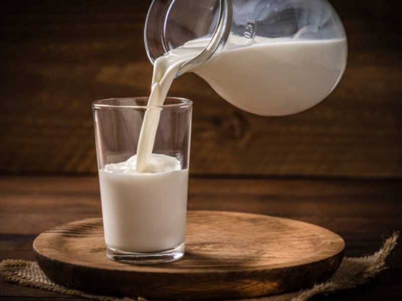 A glass of miln being filled by a pitcher of milk on a table