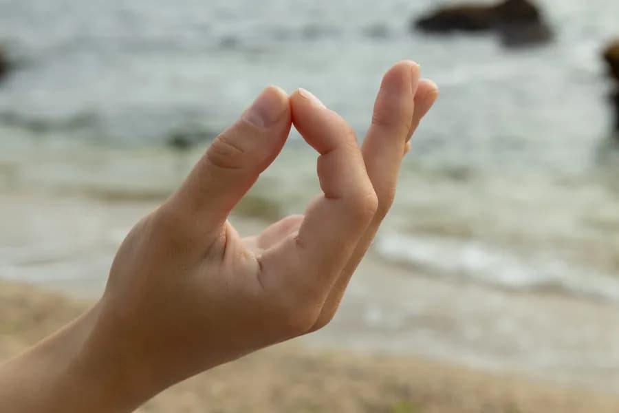 Fingers folded in Chin Maya Mudra hand gesture, seashore close-up