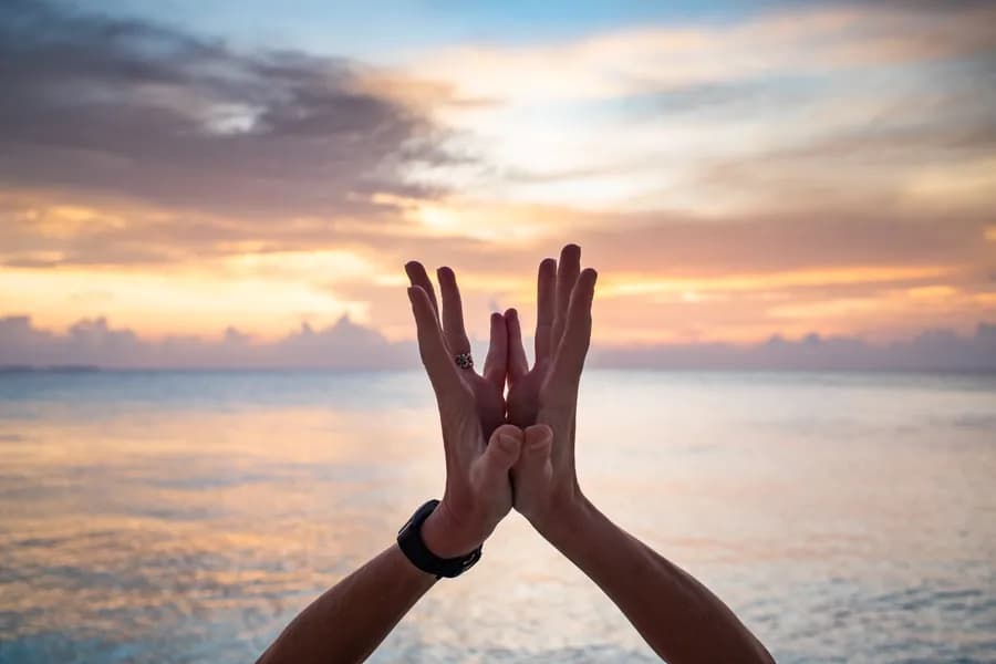 Hands forming a mudra in yoga pose at the beach during sunset