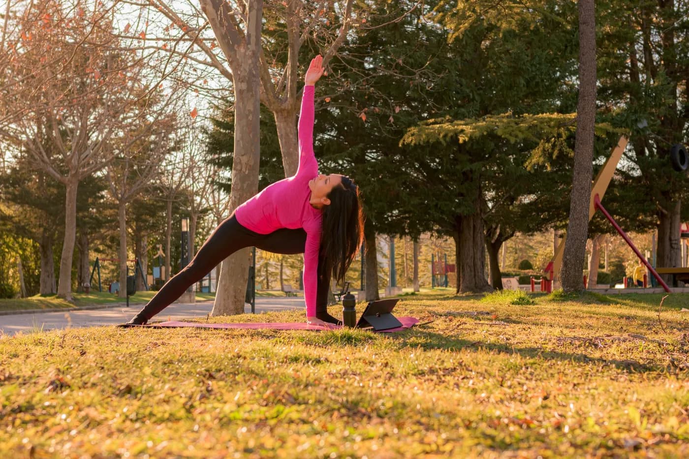 Woman performing yoga exercises in a park at sunset, practicing Parighasana (Gate Pose)