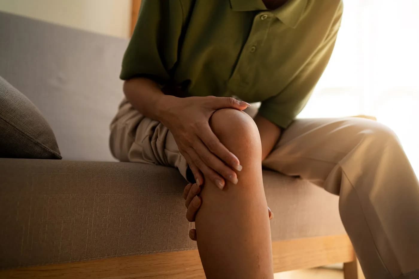 Woman massaging her sore knee while sitting on a sofa