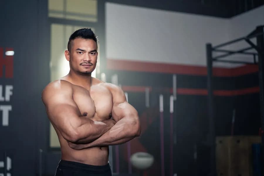 Muscular man posing with crossed arms in the gym, representing a structured workout split for muscle gain