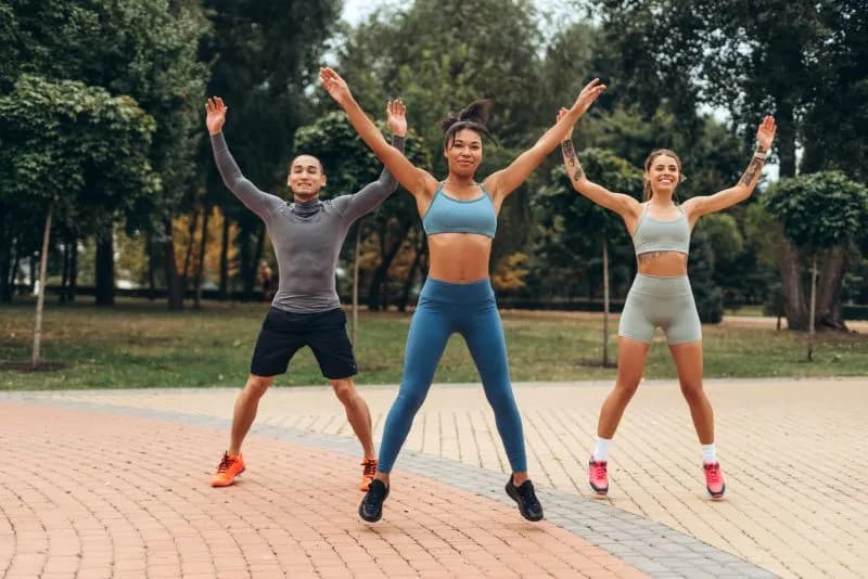Friends doing jumping jacks together outdoors as part of a fitness training routine