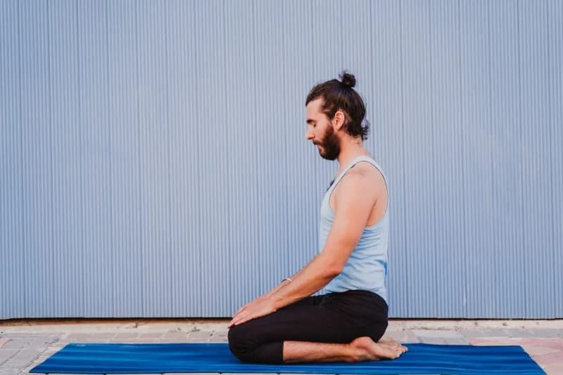 Man practicing yoga kneeling in Vajrasana pose