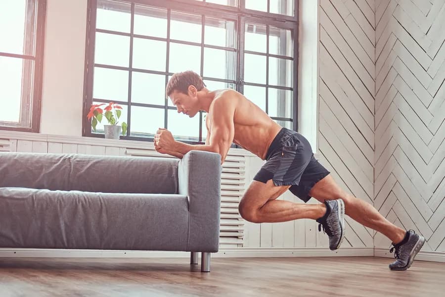Muscular man planking on a couch indoors