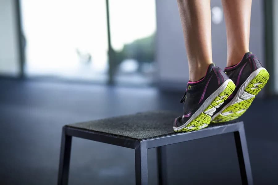 Athletic woman stepping onto an exercise box, representing calf raise training