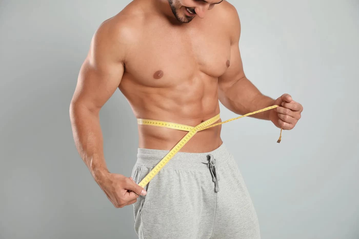 Man measuring his waist with a tape to track body recomposition progress while gaining muscle and losing fat