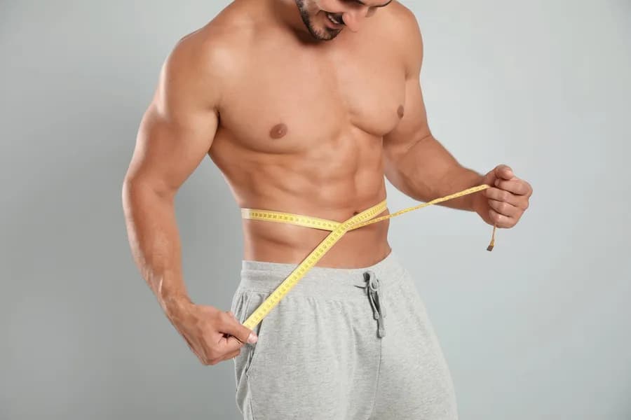 Man measuring his waist with a tape to track body recomposition progress while gaining muscle and losing fat