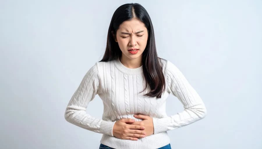Woman in a white sweater holding her stomach in discomfort, illustrating the need for stomach and core muscle strengthening