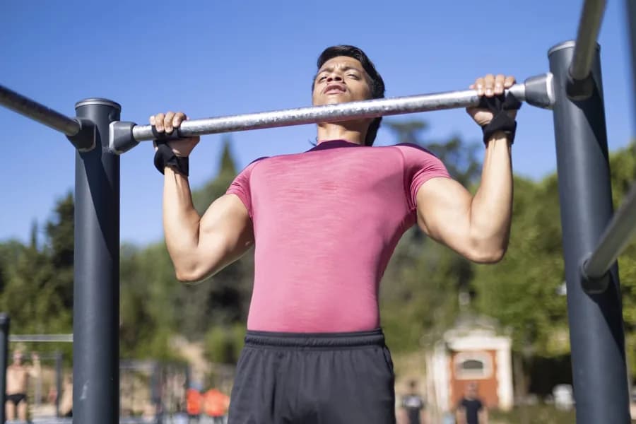 Man in pink shirt doing pull-ups on outdoor gym equipment