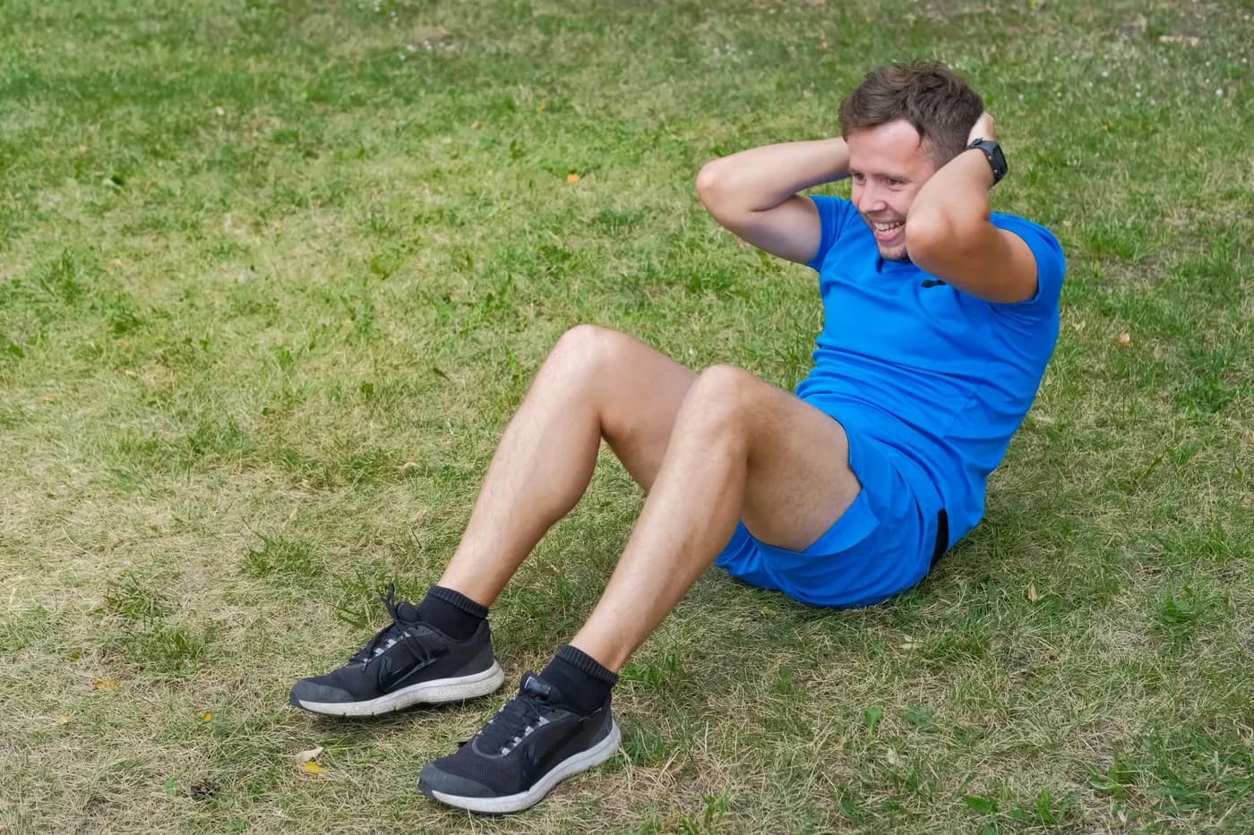 Man engaging his abdominal muscles on the grass during a strength training core workout