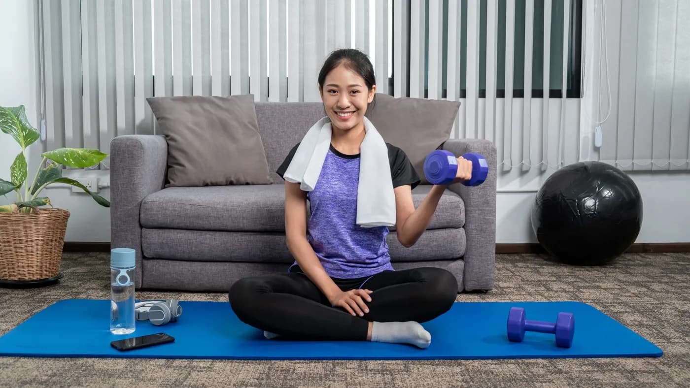 Smiling woman lifting weights at home on a yoga mat