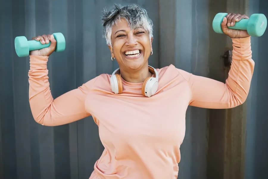 Smiling woman lifting weights outdoors on a sunny day