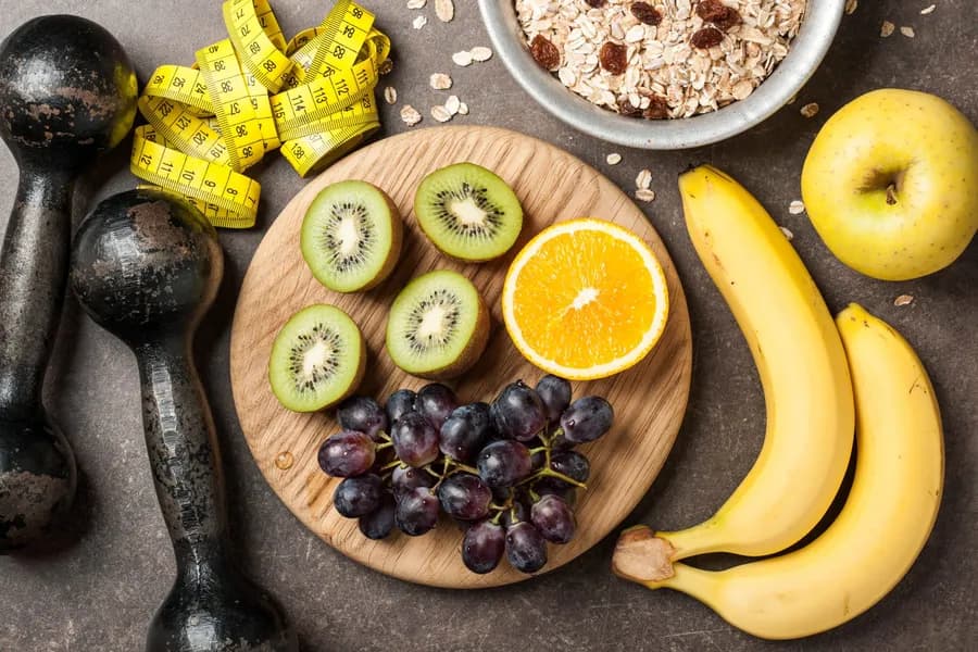 Healthy food with dumbbells on gray background
