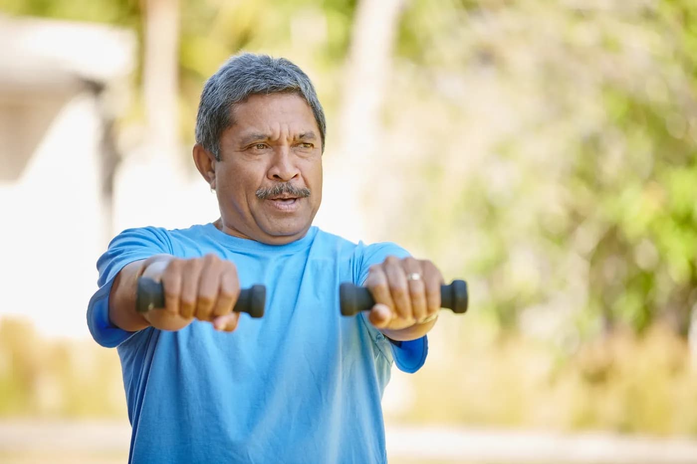 Man exercising with hand weights outdoors in the sunshine