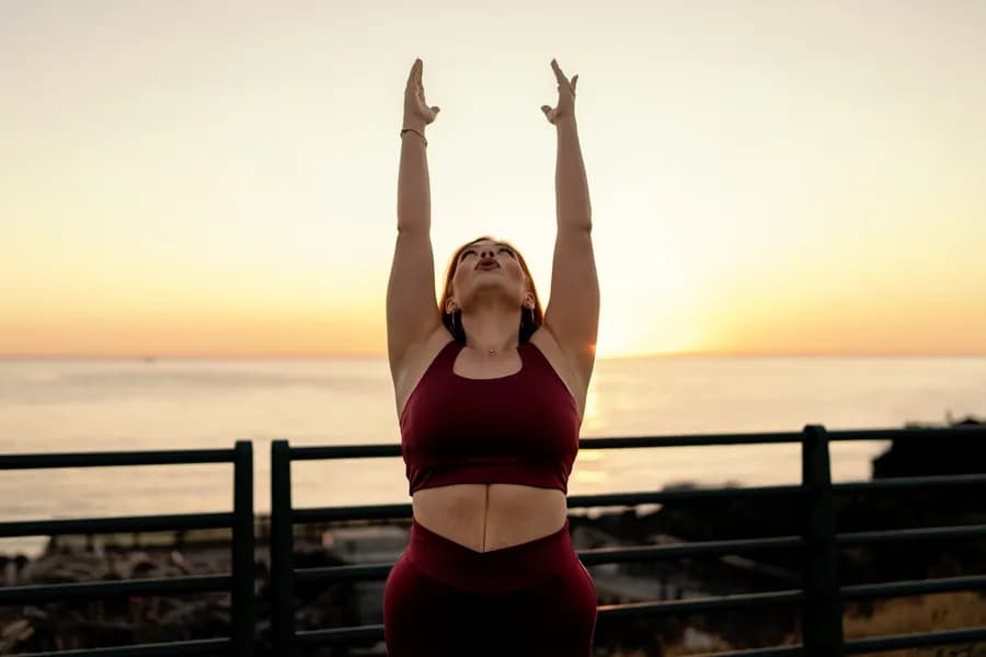 Woman stretching her arms upward at seaside sunrise before a workout