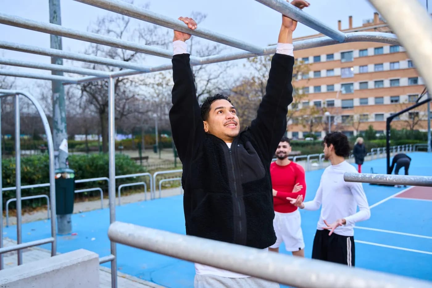 Man exercising on monkey bars outdoors with training companions