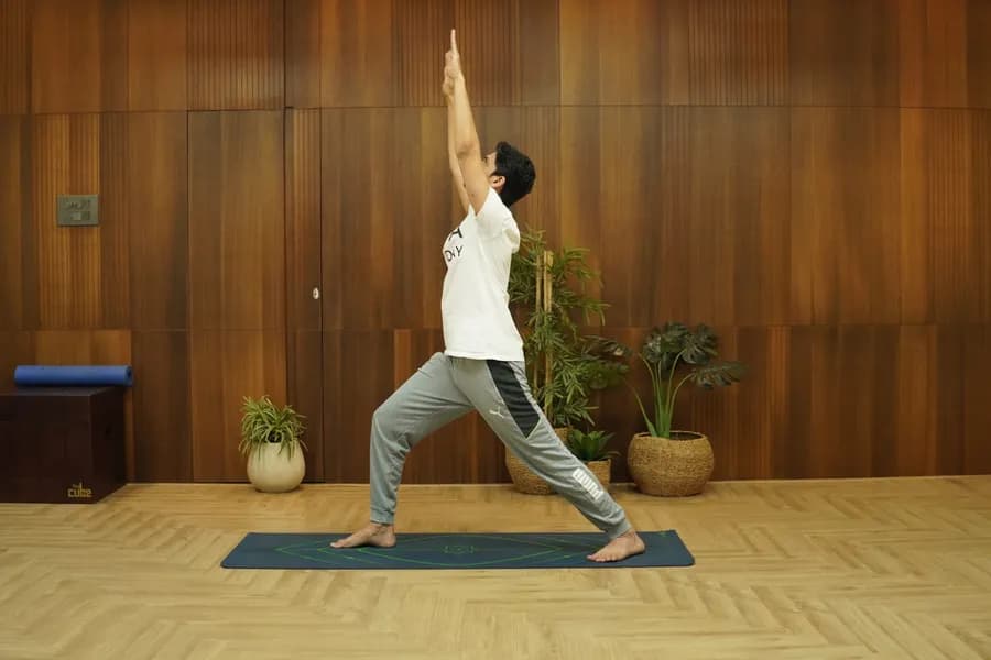 Woman demonstrating Virabhadrasana 1 (Warrior I) pose with arms raised overhead