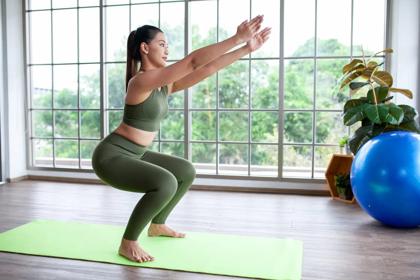 Woman doing squats on a yoga mat at home as part of a pelvic exercise routine