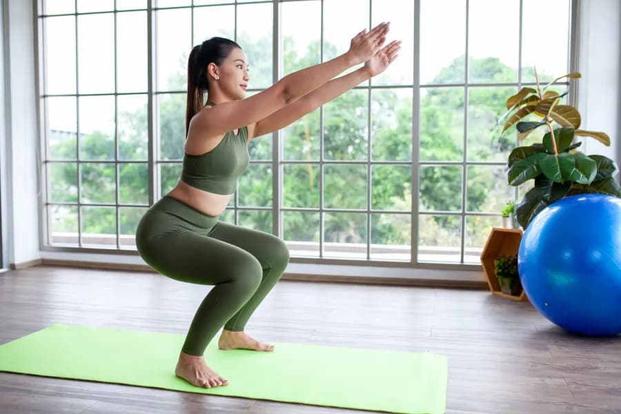 Woman doing squats on a yoga mat at home as part of a pelvic exercise routine