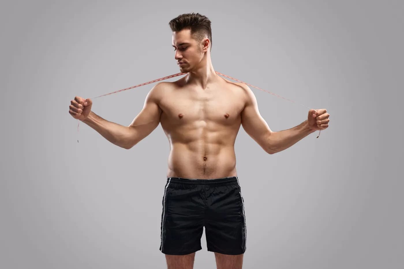 Shirtless man measuring his waist with a tape measure to track fat loss progress